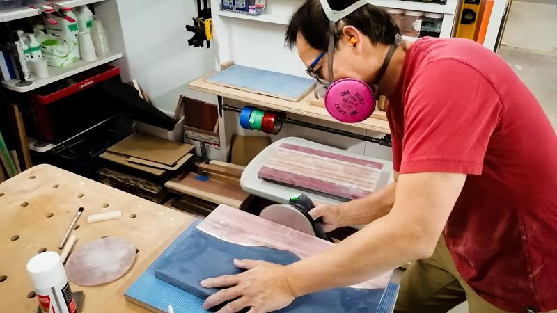 Image of a man sanding an epoxy charcuterie board with live edge wood